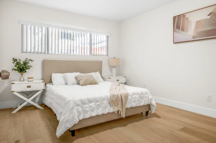 Indoor shot of a bedroom. The room is painted a beige color. The walls are smooth and matte. A large, framed abstract landscape print hangs on the wall. The floor is light laminate flooring.